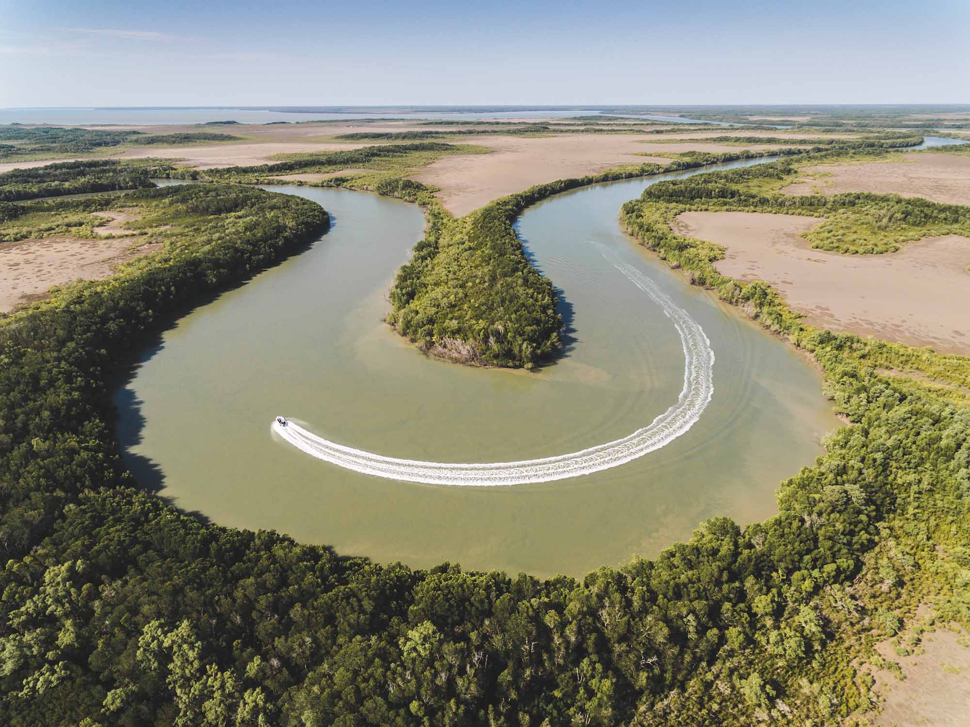 Aerial photo of a fishing boat speeding around a horse shoe shaped creek leaving behind a long wake trail in the shape of a smile